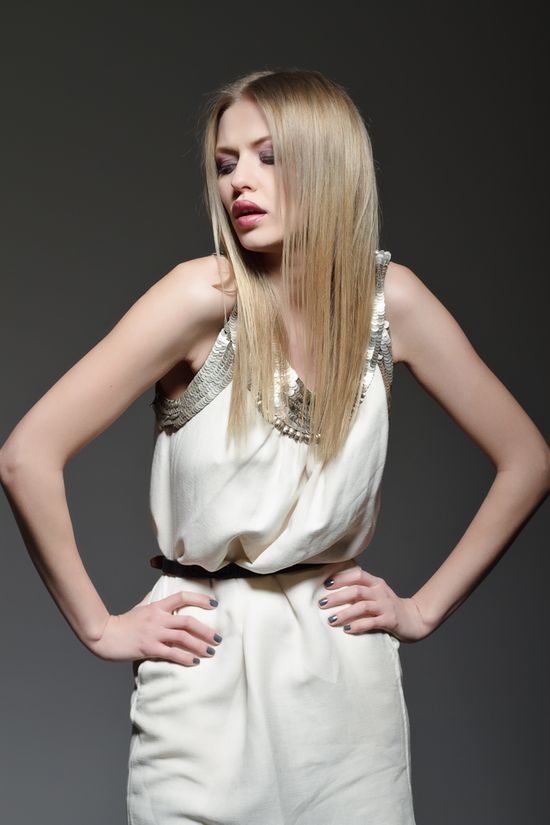 Studio fashion portrait of Simona posing in a white sleeveless dress with metallic collar detailing.
