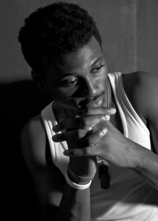 Moody black and white portrait of Josh wearing a white tank top with his hands clasped near his face.