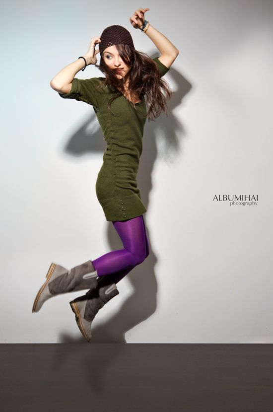 Editorial portrait of Alice captured mid-movement wearing a green knit dress and purple tights against a clean studio wall.