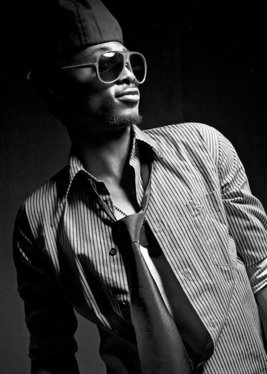 Low-key monochrome studio portrait of Josh in a striped shirt, tie, and sunglasses looking off-camera.