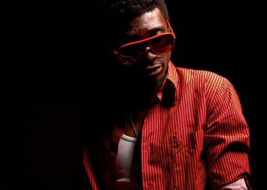 Low-key fashion portrait of Josh in a striped shirt and red sunglasses emerging from deep studio shadows.